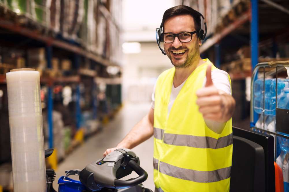 Smiling warehouse worker giving a thumbs-up while operating equipment — concept related to what is linear feet in shipping and logistics.